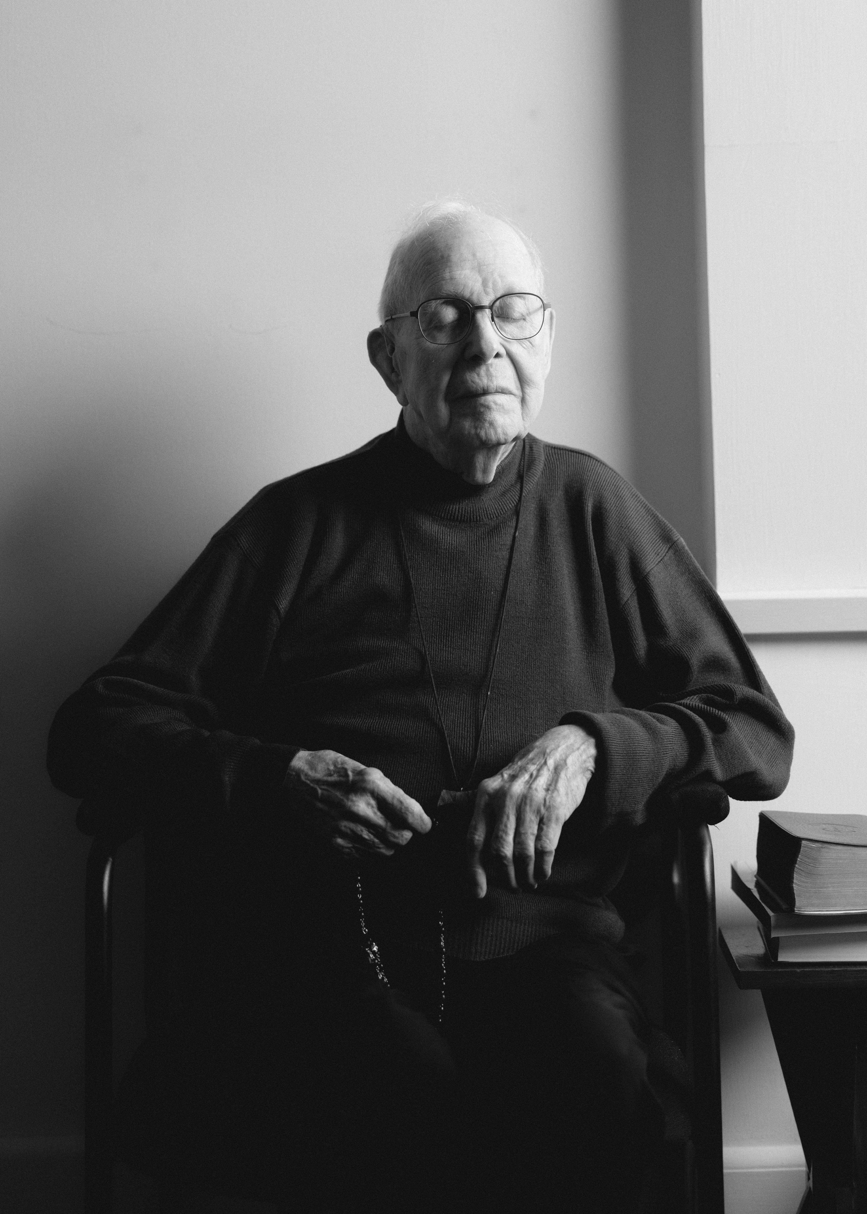 A close-up, black-and-white profile portrait of an elderly gentleman with glasses, captured in a moment of quiet contemplation. The soft, directional lighting highlights the textures of his face and the subtle drape of his dark sweater. Within this case study, this portrait exemplifies human-centered visual storytelling, using natural light and an unposed, authentic profile to communicate profound dignity, wisdom, and lived experience.