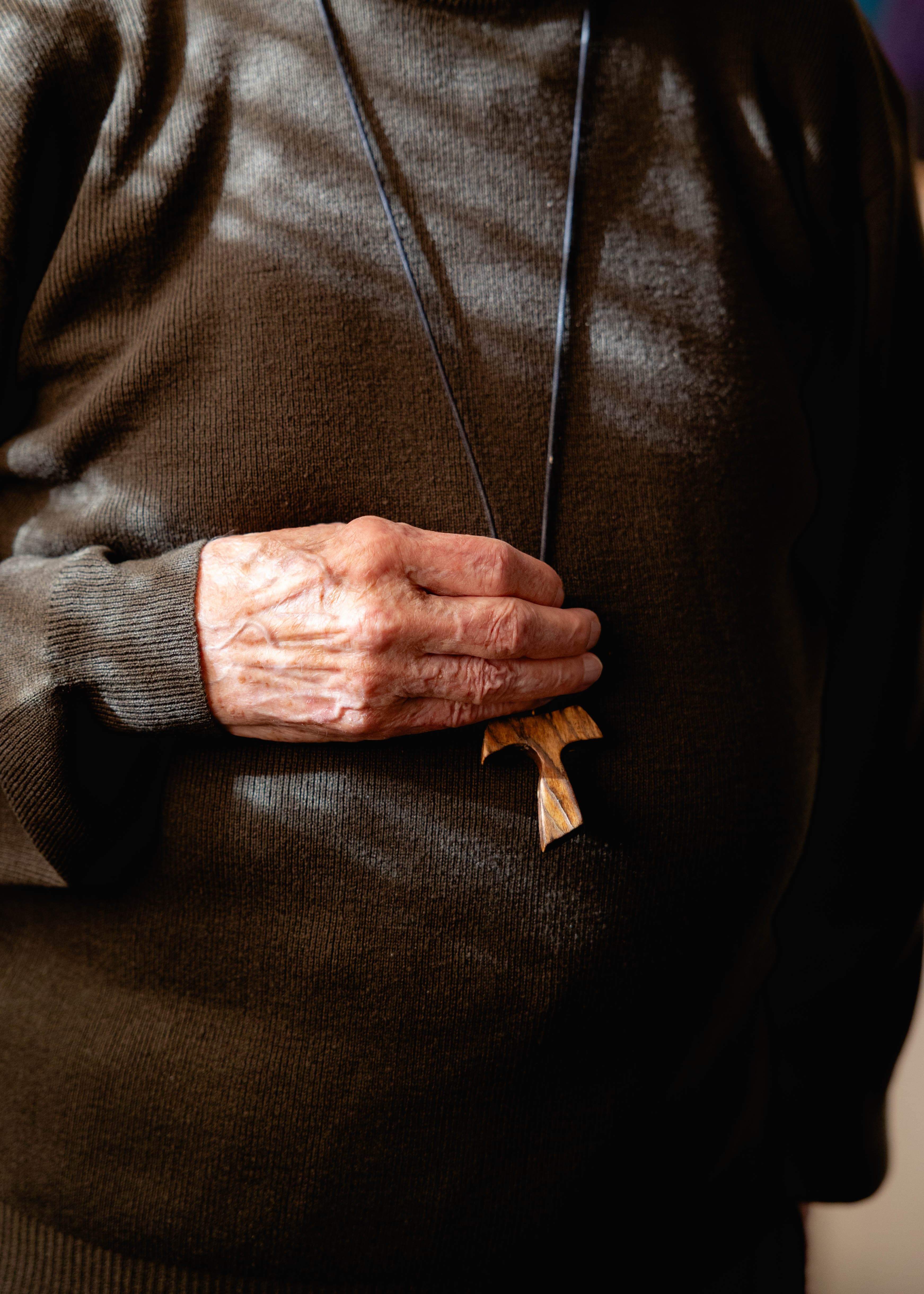 A detail shot capturing a quiet, intimate moment of a hand holding a wooden cross. This composition demonstrates visual literacy in brand photography, using tactile elements and natural light to communicate complex, deeply personal values without words.